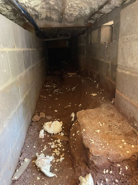 A dark, damp crawl space with exposed soil and scattered debris — the hidden problems winter brings to the surface