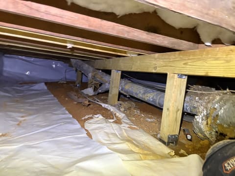 Aging crawl space beneath an older Atlanta home — exposed red-clay soil, torn vapor barrier, and deteriorating ductwork